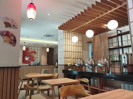 A restaurant interior with wooden furniture, a counter with food service equipment, and decorative elements like fans and a wall with a geometric pattern.