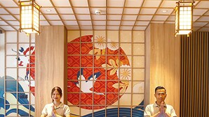 Een receptiebalie met twee personen erachter, een decoratieve muur met traditionele patronen, en een plafond met een rasterontwerp.