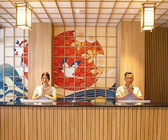 A reception desk with two individuals seated behind it, a decorative wall with traditional patterns, and a ceiling with a grid design.