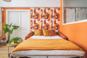 A bedroom with a bed, a patterned headboard, a potted plant, and a window.