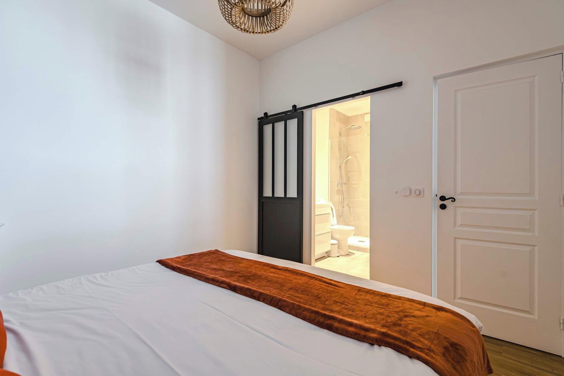 A bedroom with a bed, a door, and a view of a bathroom.