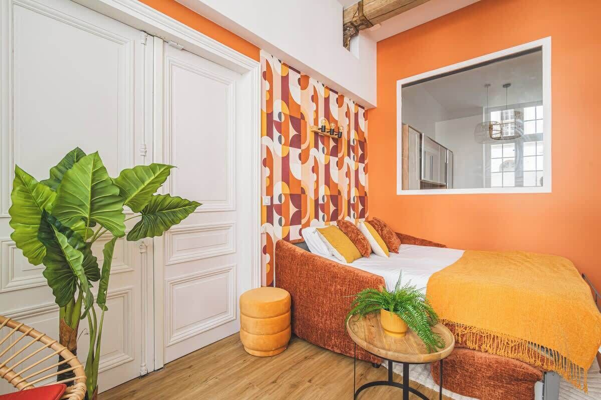 Una habitación con una cama, un espejo, una planta y un taburete redondo.
