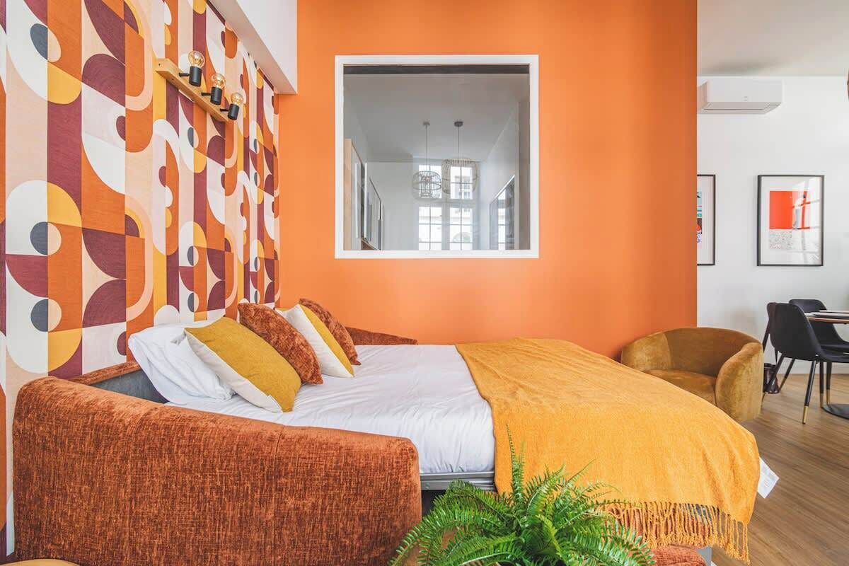 A modern hotel room with a large bed, a sofa, a small table, and a potted plant.