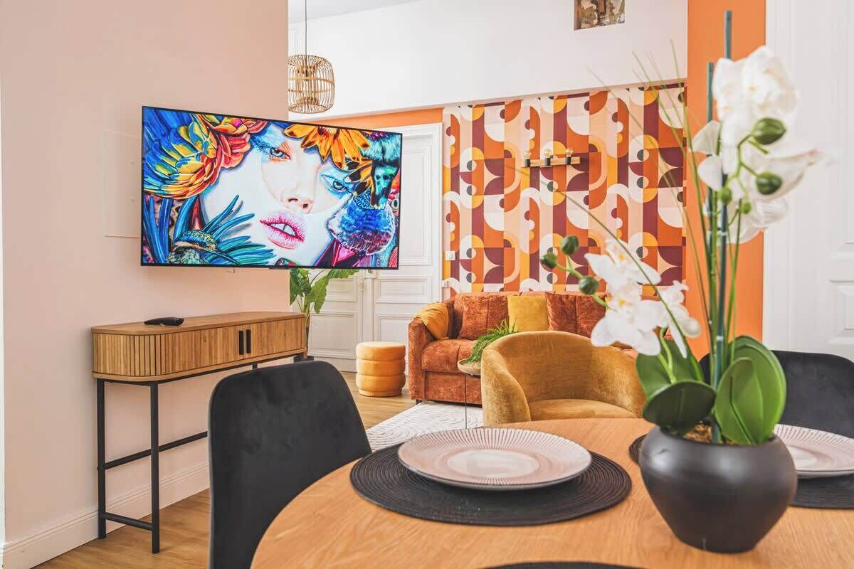 A dining area with a round table, chairs, a television mounted on the wall, and a patterned wall in the background.