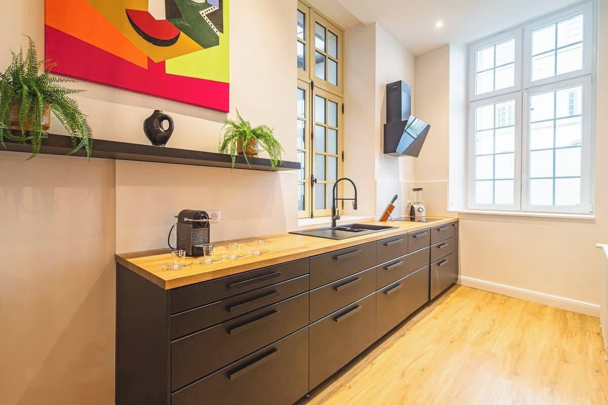 A modern kitchen with a wooden countertop, black cabinets, a built-in sink, and a large window providing natural light.