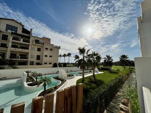 Un espace piscine au design incurvé, entouré de palmiers et d’une pelouse bien entretenue.