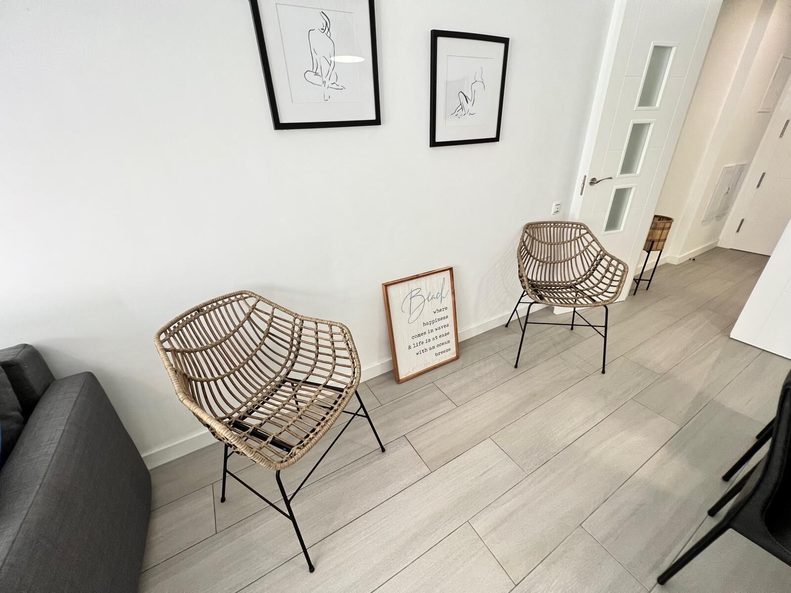 A modern living room with two wicker chairs, a grey sofa, and two framed artworks on the wall.