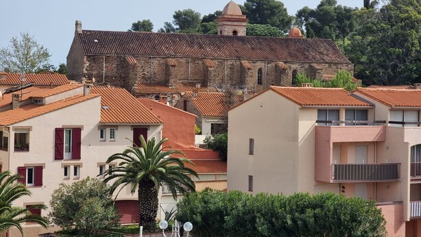 Un edificio histórico con una cúpula y un campanario, rodeado de edificios residenciales con tejados de tejas rojas.