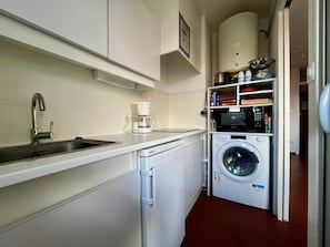 Ett kompakt kök med diskho, kaffebryggare, mikrovågsugn och tvättmaskin.
