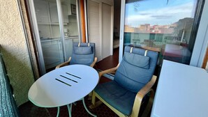 Un balcón con una mesa y dos sillas, una puerta corrediza de vidrio y vistas a edificios.