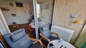 Una habitación con dos sofás azules, una mesita redonda con una taza, y vistas a otra habitación con una cama y una pequeña mesa a través de un ventanal.