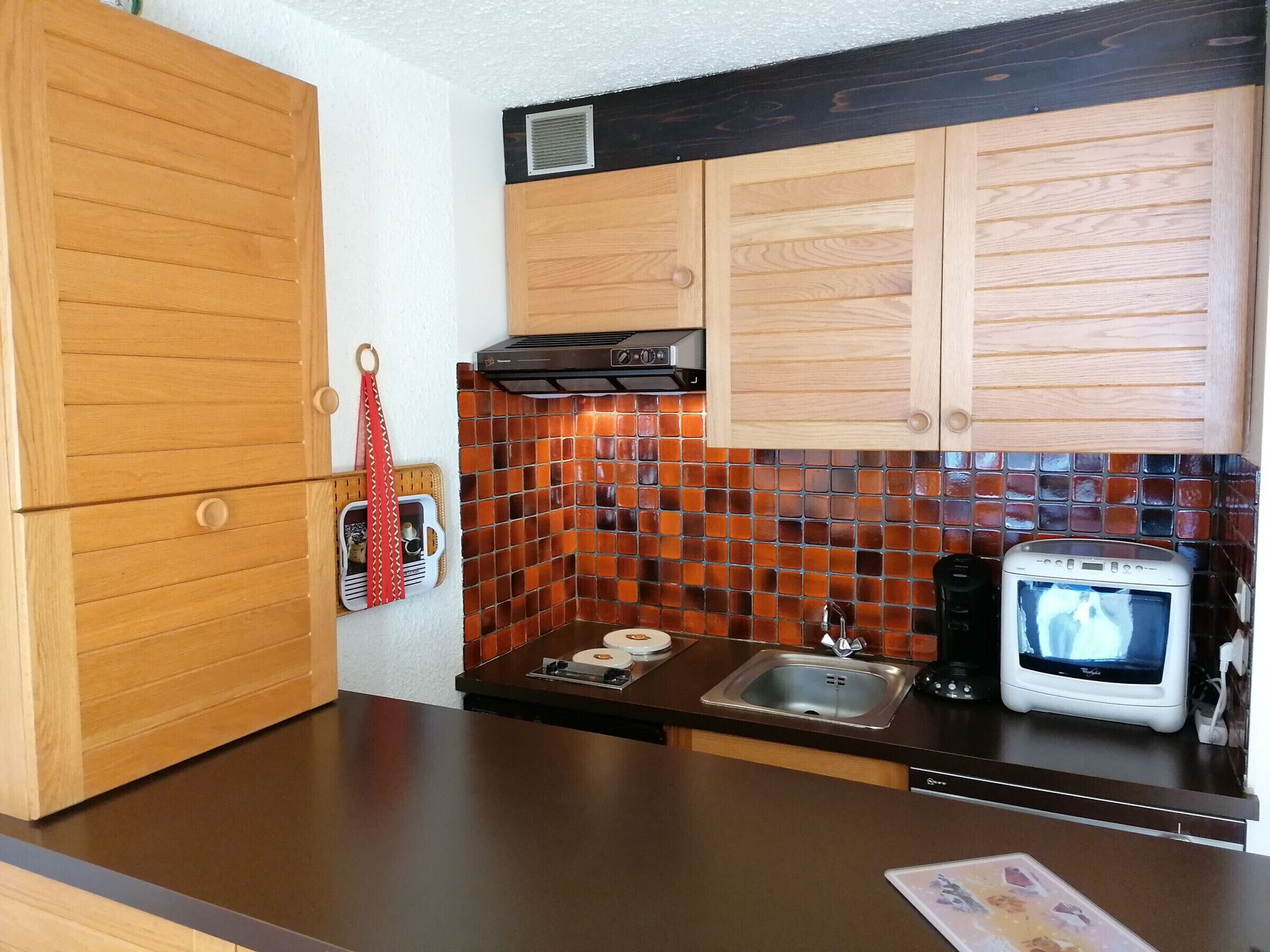 A kitchen with wooden cabinets, a tiled backsplash, a microwave, and a sink.
