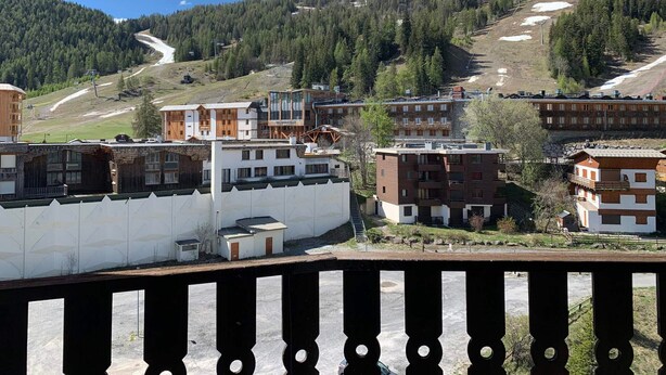 Eine gebirgige Landschaft mit Gebäuden, darunter ein mehrstöckiges Hotel und eine Skipiste im Hintergrund.