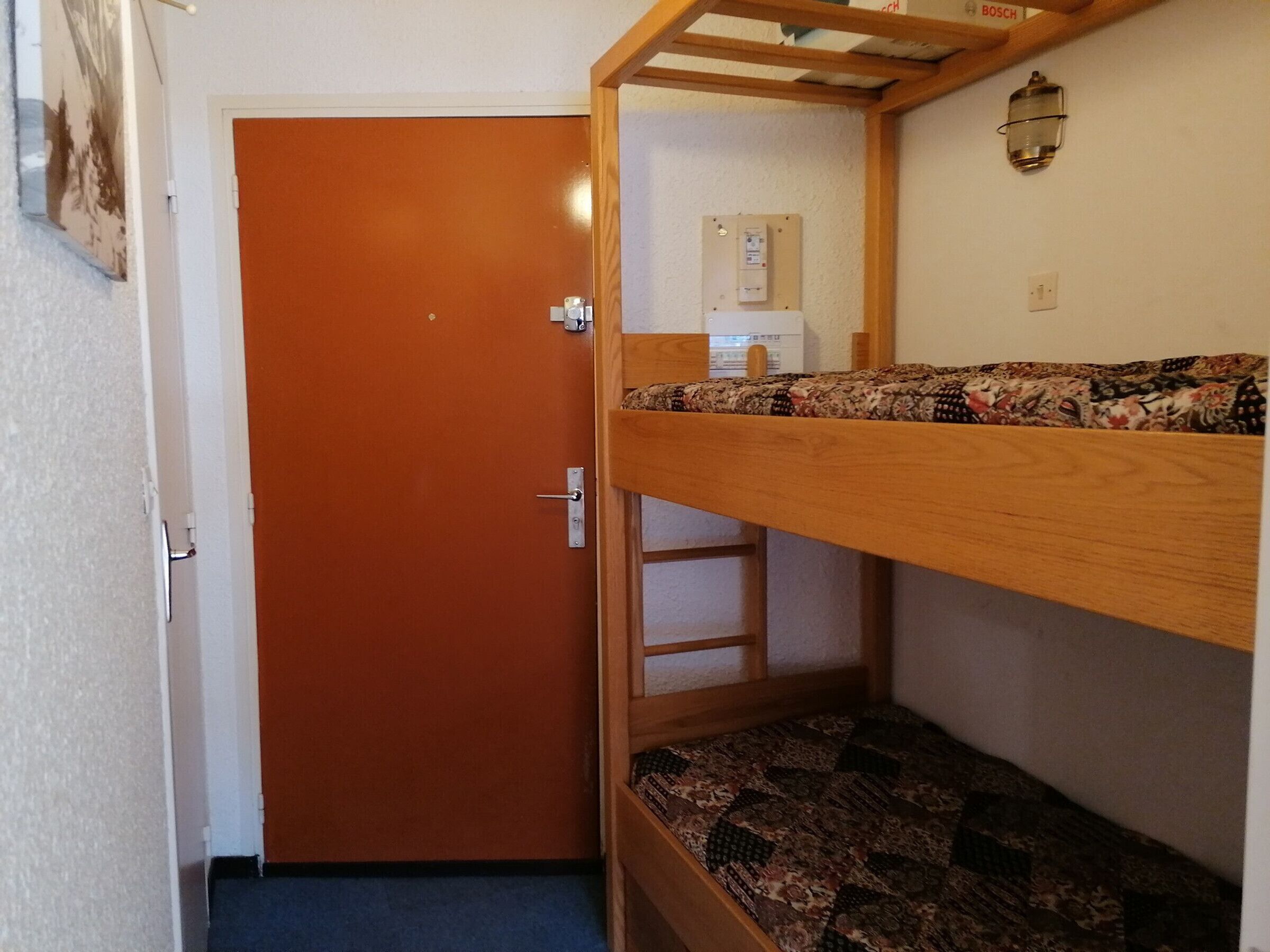Una cama individual superpuesta con un colchón estampado, una escalera de madera y una puerta con pomo.