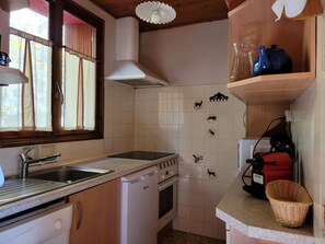 A compact kitchen with a sink, stove, and oven, wooden cabinets, a window with curtains, and a ceiling fan. - Cozy chalet for 9, large balcony, near slopes, private parking (Pra-Loup)