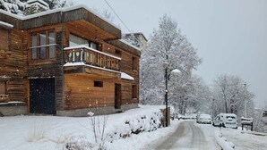 En træhytte med balkon, grusvej og snærede omgivelser.