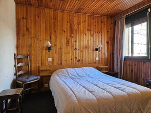 A wooden-paneled room with a bed, two wall-mounted lamps, a chair, and a window. - Cozy chalet for 9, large balcony, near slopes, private parking (Pra-Loup)