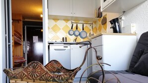 Una cocina compacta con lavavajillas, un colgador para ollas y una cesta de mimbre con estructura metálica.