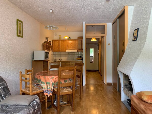 A cozy living room with a fireplace, a dining area with wooden furniture, and a kitchen with wooden cabinets and a microwave.