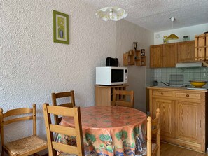 A compact kitchen with wooden cabinets, a microwave, and a dining table with chairs.