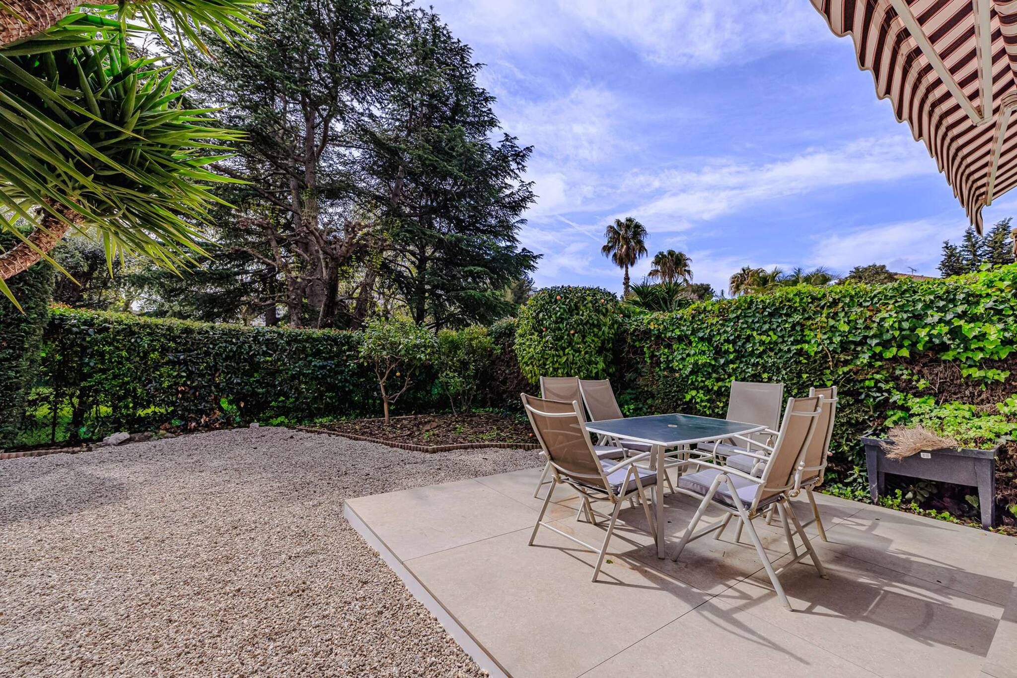 Une terrasse extérieure avec une table et des chaises, entourée de verdure et d’arbres.