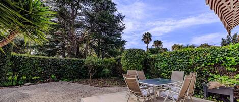Une terrasse extérieure avec une table et des chaises, entourée de verdure et d’arbres.