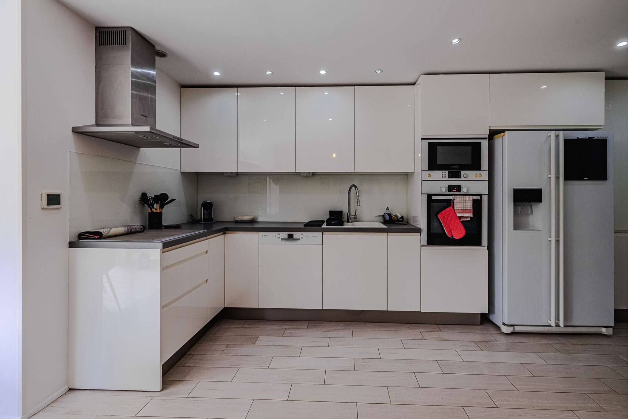 A modern kitchen with white cabinets, a stainless steel range hood, a microwave, an oven, and a refrigerator.