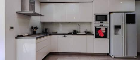 A modern kitchen with white cabinets, a stainless steel range hood, a microwave, an oven, and a refrigerator.