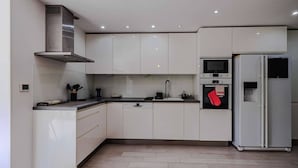 A modern kitchen with white cabinets, a stainless steel range hood, a microwave, an oven, and a refrigerator. - Marina Rey – 400m from beach, Côte d’Azur vibe (Villeneuve-Loubet)