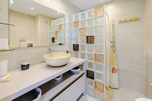 Un baño moderno con un espejo grande, un lavabo blanco y una pared divisoria de vidrio.