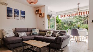 A modern living room with a sectional sofa, a coffee table, and a dining area with a table and chairs. There are three wall-mounted artworks and a hanging light fixture. - Marina Rey – 400m from beach, Côte d’Azur vibe (Villeneuve-Loubet)