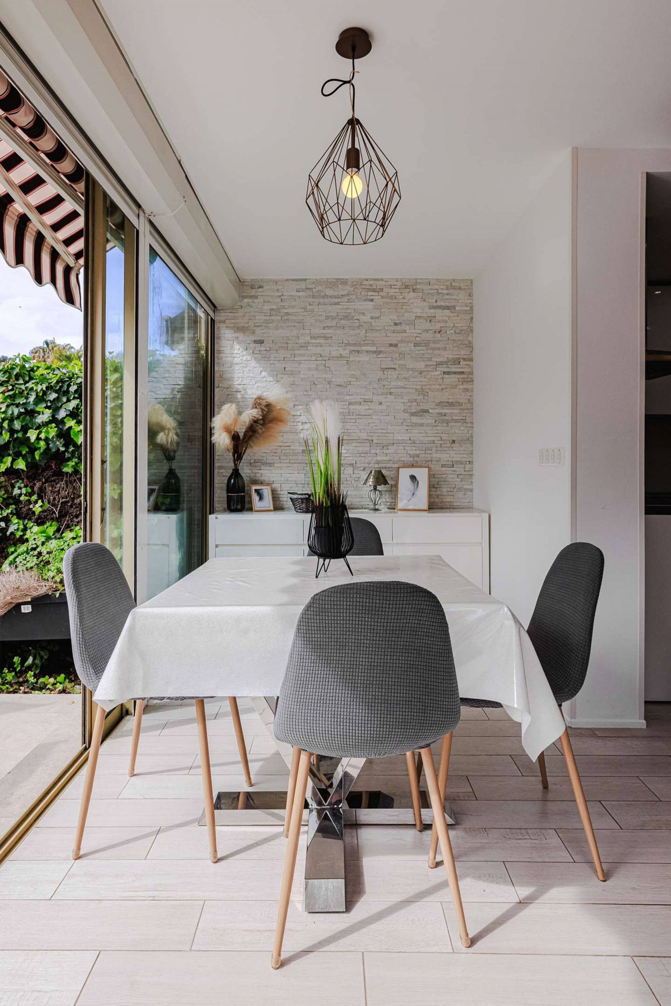 Un espace repas moderne avec une table blanche, quatre chaises et un luminaire suspendu.