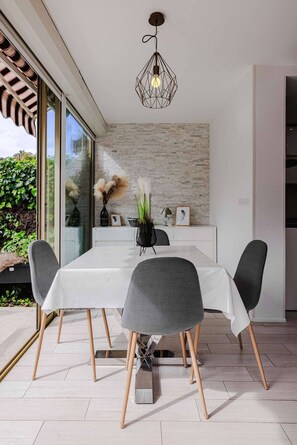 A modern dining area with a white table, four chairs, and a hanging light fixture. - Marina Rey – 400m from beach, Côte d’Azur vibe (Villeneuve-Loubet)