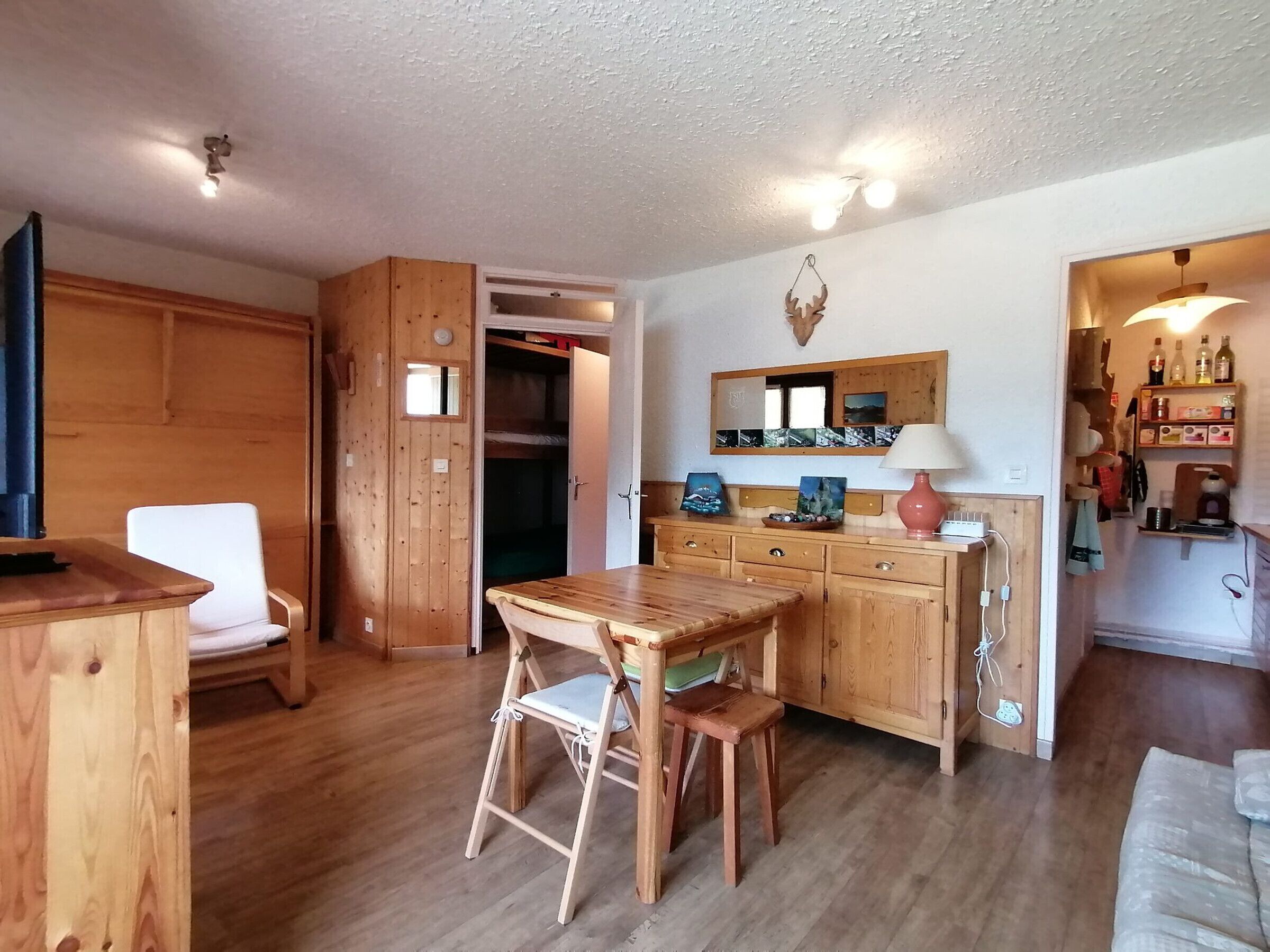 Une pièce chaleureuse, meublée de meubles en bois, avec une table à manger, un banc et un coin cuisine agrémenté d’un miroir et d’étagères.