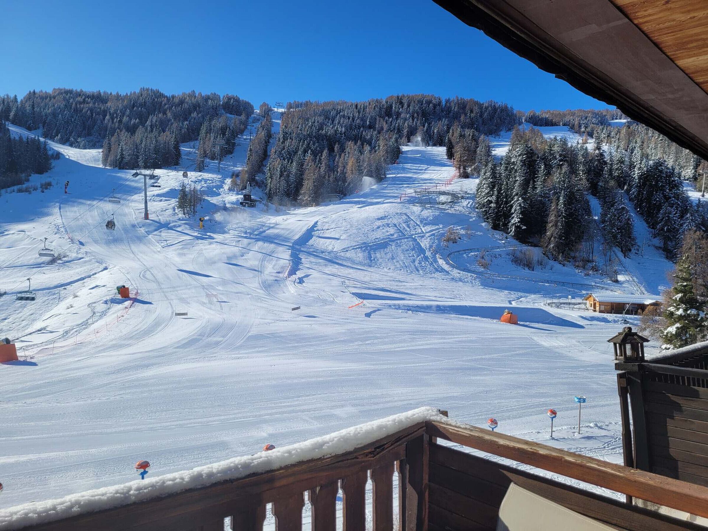 Ein verschneiter Skipisten mit einer Holzhütte und einer Seilbahn im Hintergrund.