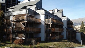 En bygning med flere etager, træbalkoner, en stenfacade og et bjergrigt landskab i baggrunden.