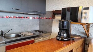 A kitchen with grey cabinets, a stainless steel sink, a gas stove, a coffee maker, and a microwave on a wooden stand.