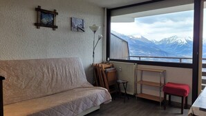 A cozy room with a sofa, a small table, and a view of snow-capped mountains through a large window.