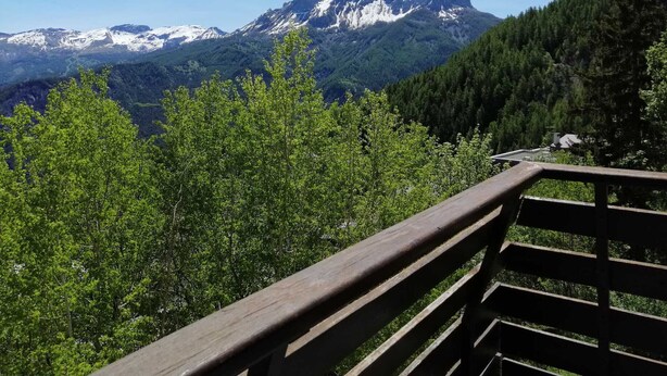 A wooden bench overlooking a mountainous landscape with snow-capped peaks and dense forest.
