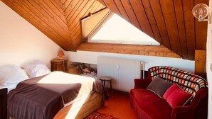 A bedroom with a sloped wooden ceiling, a bed, a red sofa, a small table, and a radiator. - 2-room apartment for 4, balconies, mountain view, parking (Pra-Loup)