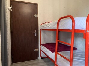 A bunk bed with a red frame and white bedding, a wooden door with a silver handle, and a white textured wall.