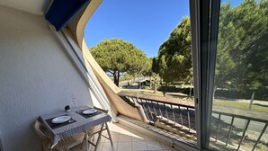 A balcony with a dining table set for two, a view of a park, and a clear blue sky. - Charming Studio for 4 with Sea View, Pool, and Parking Near the Beach (Le Grau-du-Roi)