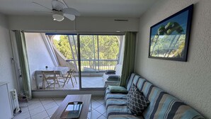 A room with a sofa, a table, a ceiling fan, a window, and a balcony. - Charming Studio for 4 with Sea View, Pool, and Parking Near the Beach (Le Grau-du-Roi)