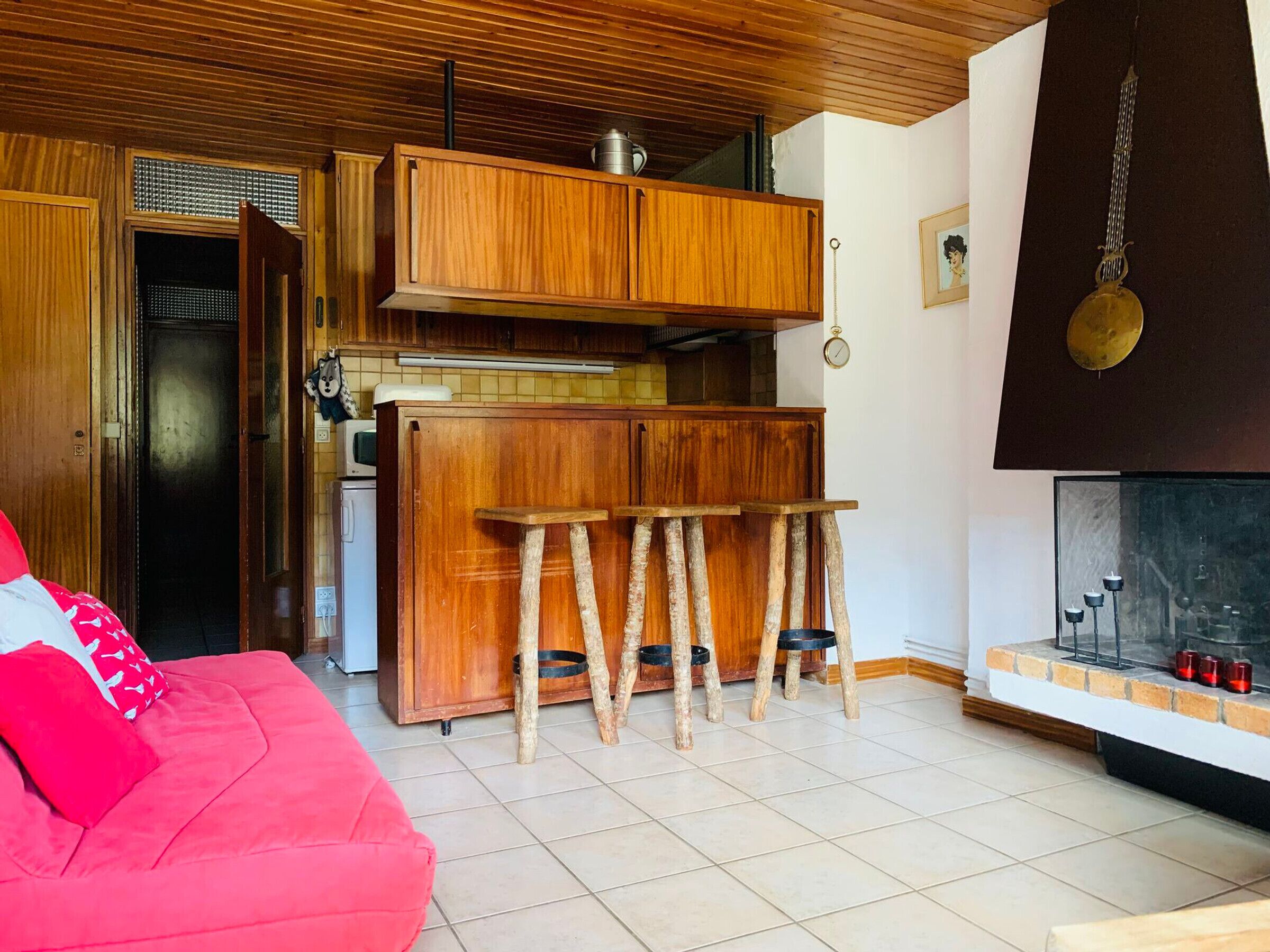 A compact living space with a kitchenette, a red sofa, and a hanging pot rack.