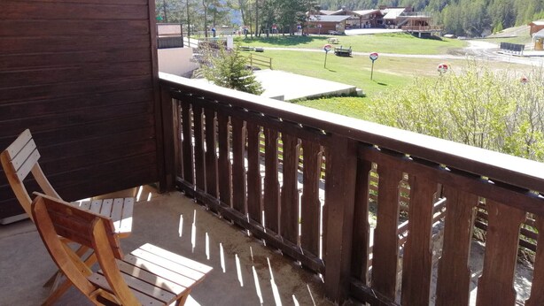 A wooden deck with a view of a mountain landscape, a wooden chair, and a building with a sloped roof.
