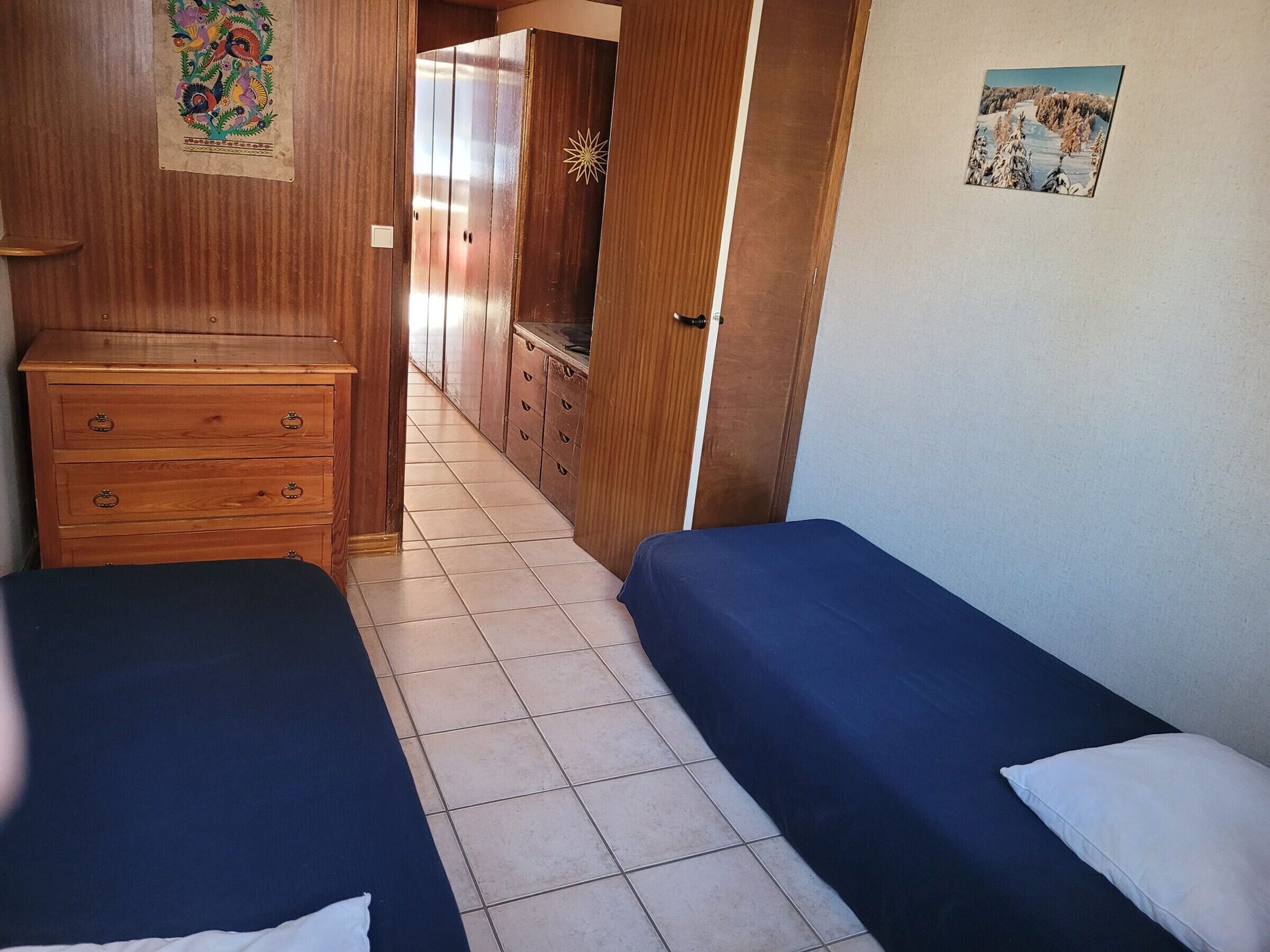 A room with two beds, wooden furniture, and a tiled floor.