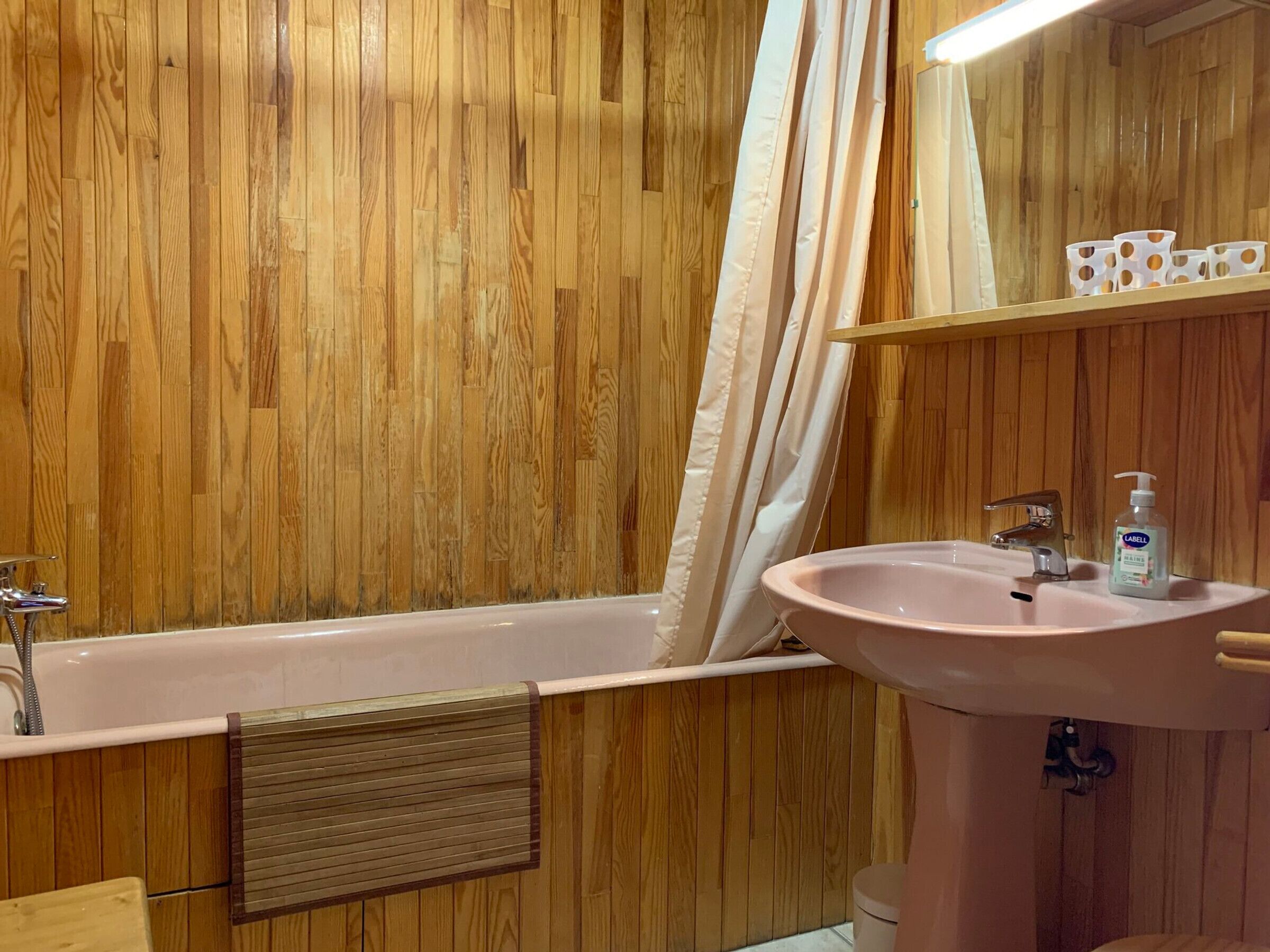 A bathroom with a wooden wall, a bathtub, a sink, and a mirror.