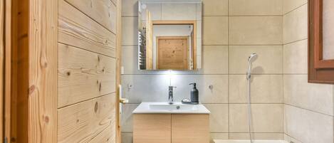 A modern bathroom with wooden cabinetry, a white sink, a mirror, and a shower.