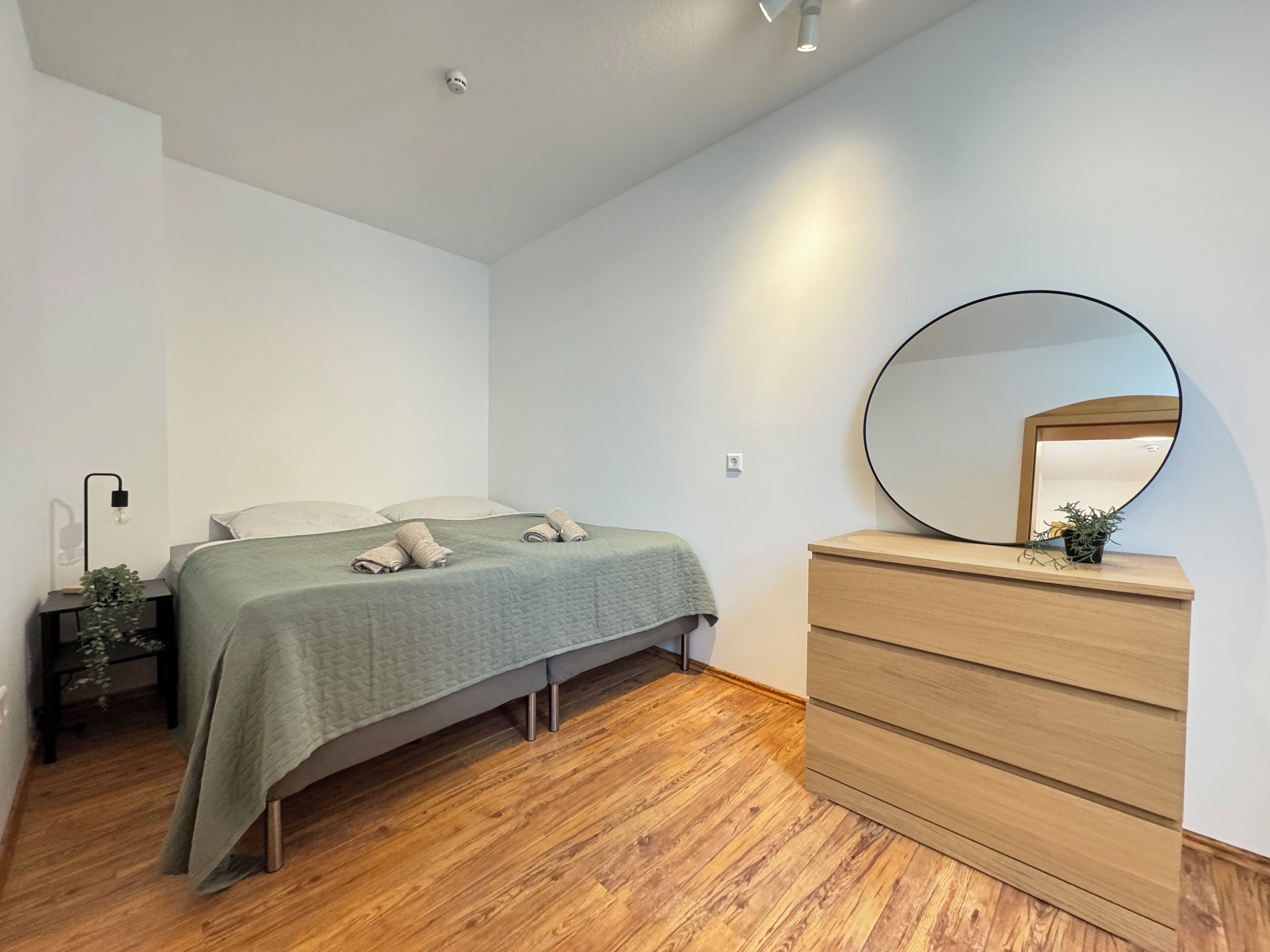 Un dormitorio con cama, cómoda, espejo y mesita de noche con lámpara.