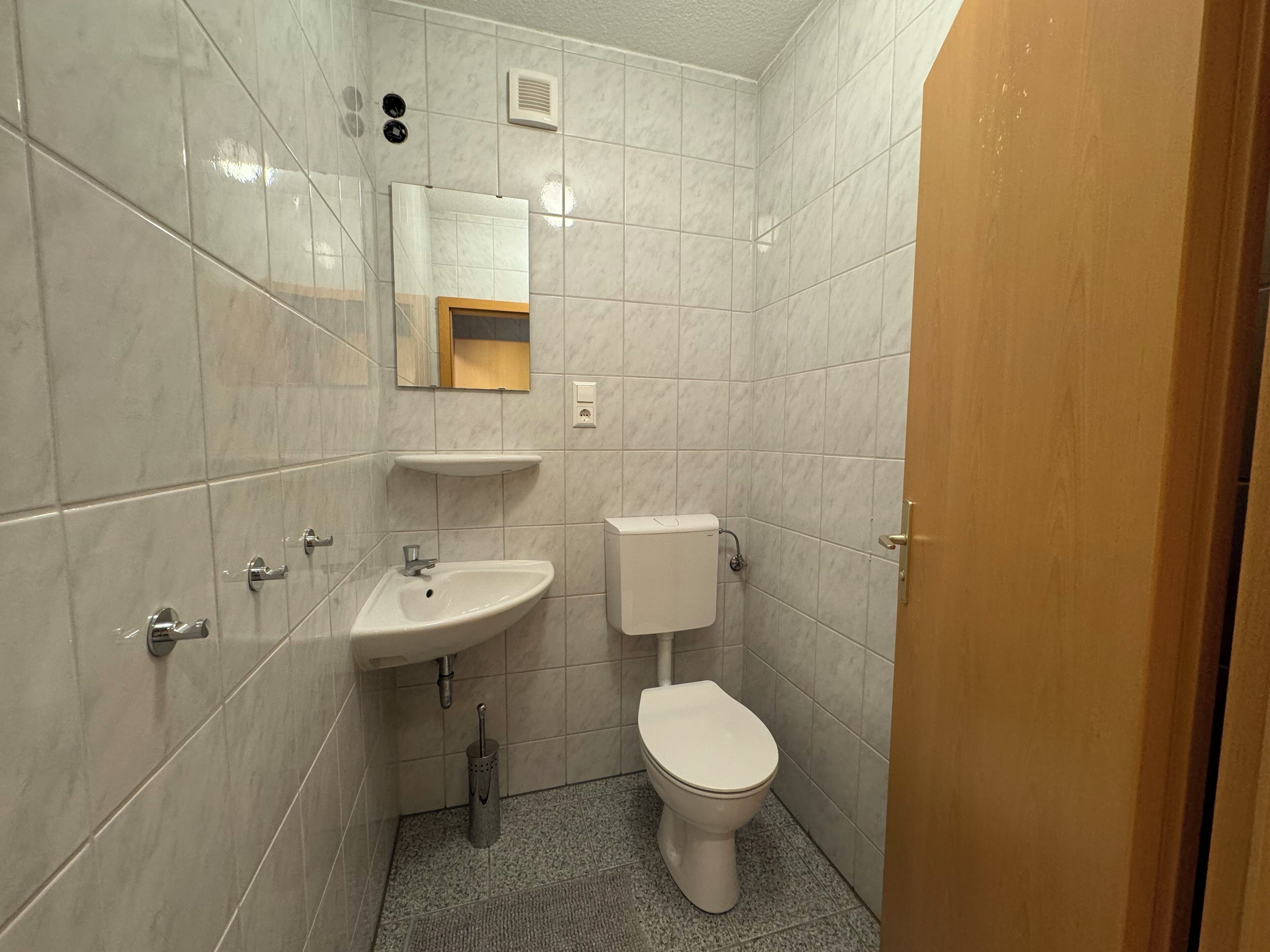 Een kleine, schone badkamer met witte tegels, een wastafel, toilet en spiegel.